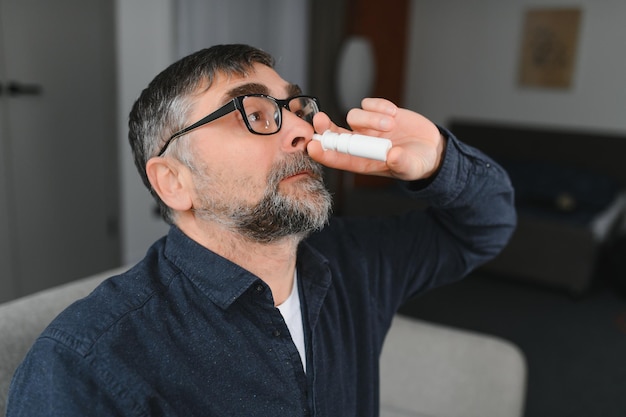 Enfermedad y enfermedad Primer plano de un hombre que se siente enfermo Gotas nasales goteantes en la nariz bloqueada Retrato masculino Sprays para el resfriado y la medicina del seno en el tratamiento de la sinusitis de la nariz que cae