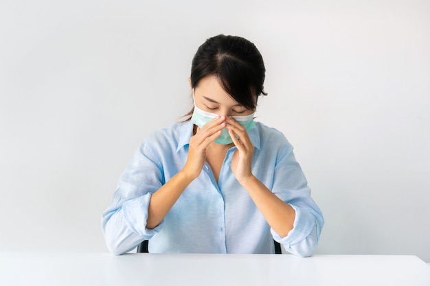 Enfermedad Muchacha asiática que lleva una mascarilla médica que se sienta en casa sobre blanco.