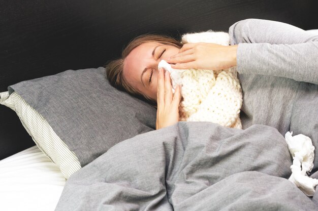 Foto enfermedad. tratamiento a domicilio. la mujer joven está enferma en casa, secreción nasal y gripe