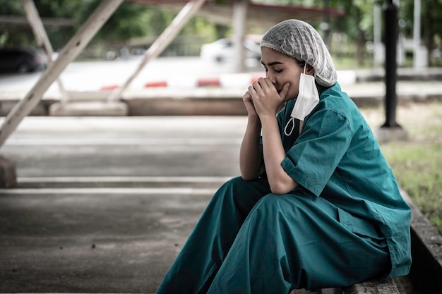 Enfermeira asiática deprimida cansada usa máscara facial uniforme azul senta-se no chão do hospital Jovem médica estressada pelo trabalho duro