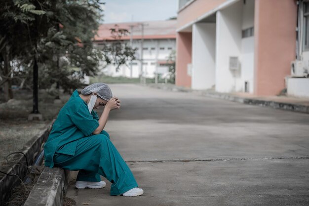 Enfermeira asiática deprimida cansada usa máscara facial uniforme azul senta-se no chão do hospital Jovem médica estressada pelo trabalho duro