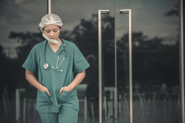 Enfermeira asiática deprimida, cansada, usa máscara facial, uniforme azul, senta-se no chão do hospital, médica jovem, estressada com o trabalho duro.