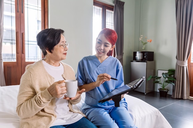Enfermeira asiática vestindo roupa médica relata o estado de saúde de uma mulher asiática sênior com um tablet digital