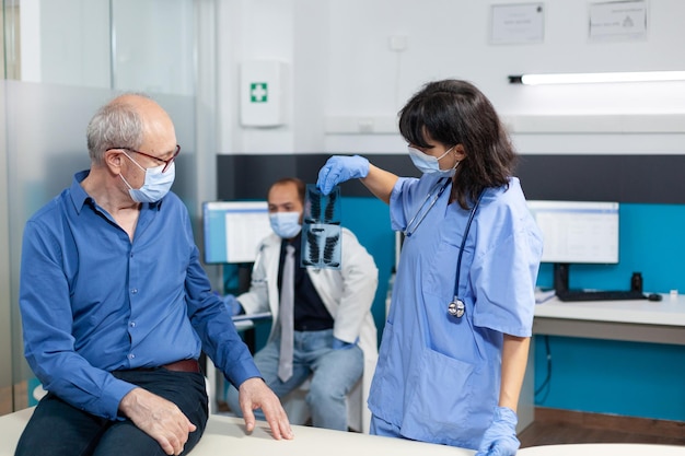 Enfermeira com máscara facial segurando radiografia de paciente idoso