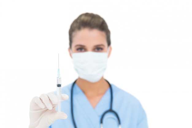 Enfermeira de cabelos lindos em azul esfrega usando uma máscara de proteção e segurando uma seringa