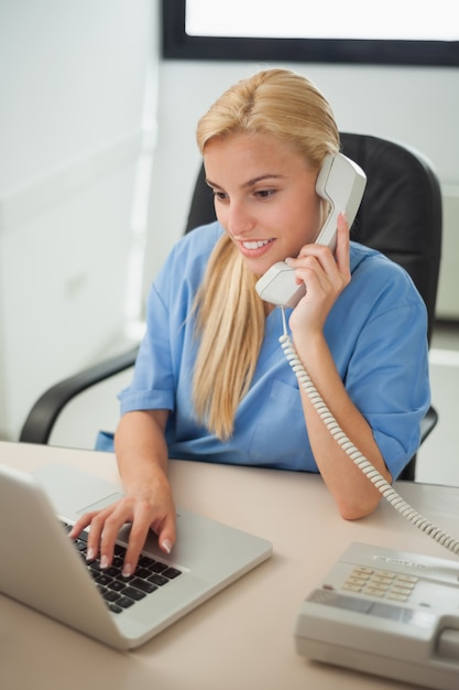 Enfermeira digitando em um laptop enquanto segura um telefone