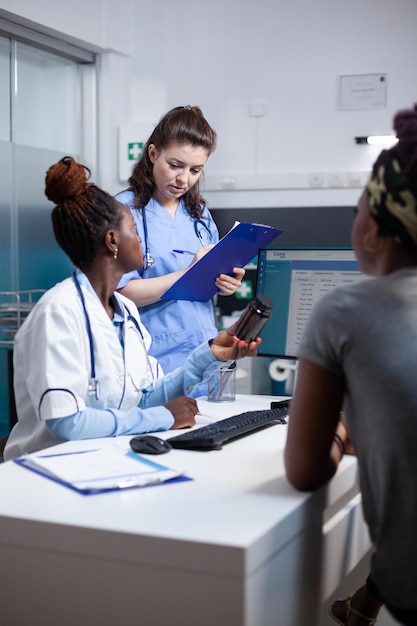 Foto enfermeira e médico discutindo as melhores opções médicas para o paciente no consultório da clínica durante a consulta. clínico geral prescrevendo remédio em garrafa para mulher afro-americana