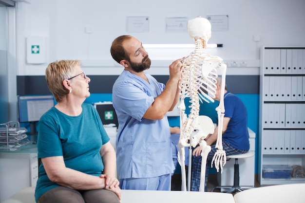 Enfermeira e paciente aposentado olhando para a medula espinhal em esqueleto humano para exame osteopático Assistente médico apontando para os ossos da coluna vertebral para explicar o diagnóstico para mulher sênior para cuidados de saúde