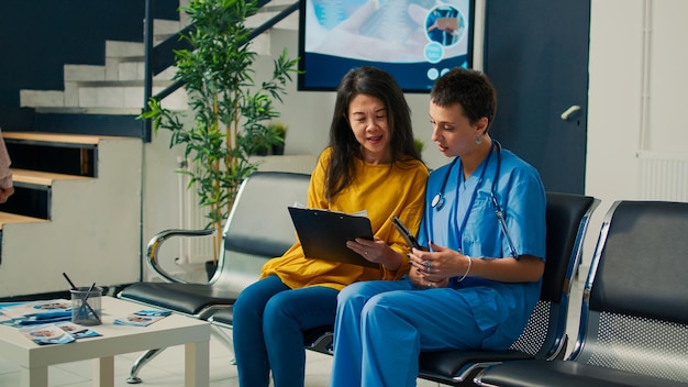 Enfermeira e paciente asiático fazendo consulta médica, analisando documentos de relatório de verificação. Usando tablet digital na hora marcada no lobby da sala de espera, falando sobre suporte de saúde.