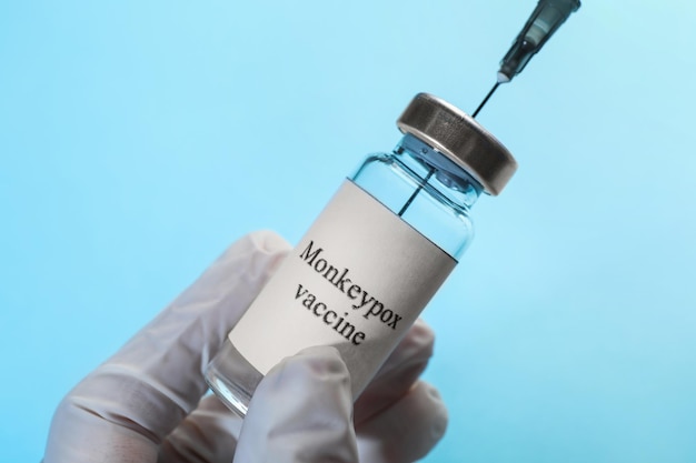 Enfermeira enchendo a seringa com a vacina da varíola dos macacos do frasco sobre fundo azul claro closeup