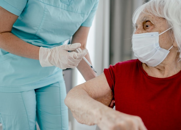 Enfermeira faz a injeção na mão de uma mulher idosa na máscara durante a pandemia. Garota trabalhadora de saúde se preocupa com uma pessoa idosa e foi baleada em um momento ambicioso