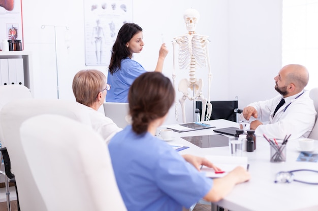 Foto enfermeira fazendo apresentação na frente da equipe de médicos sobre anatomia humana usando esqueleto. terapeuta especialista em clínica falando com colegas sobre doenças, profissional de medicina.