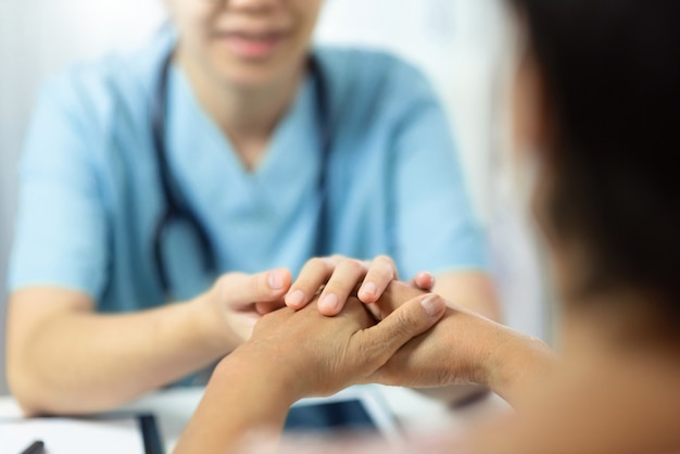 Foto enfermeira médica asiática que fala e que consola o paciente superior da mulher na sala do escritório. idoso do sexo feminino sendo tranquilizado pelo médico com as mãos