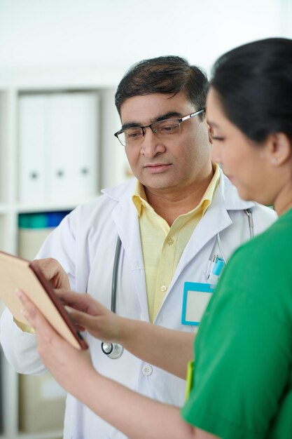 Foto enfermeira médica mostrando computador tablet com resultados de exames médicos de paciente para colega