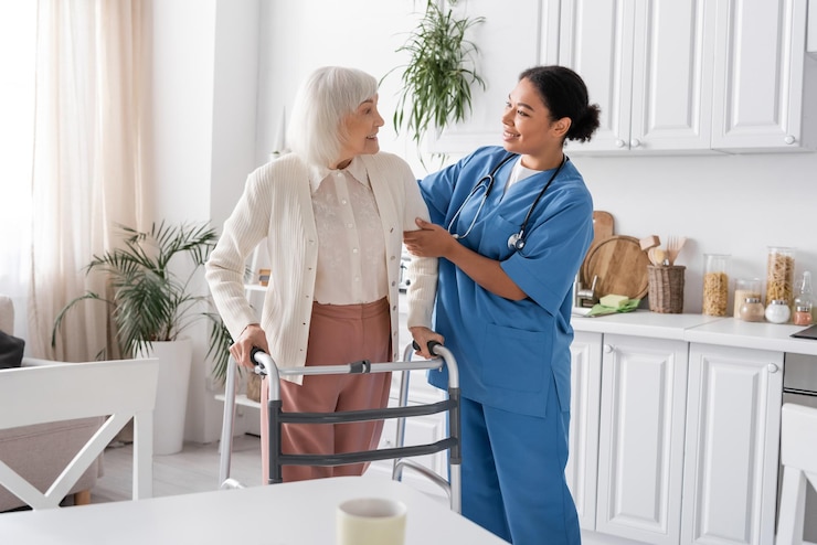 Foto enfermeira multi-racial feliz em uniforme azul apoiando mulher idosa com cabelo cinzento caminhando com a ajuda de