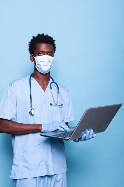 Enfermeira negra segurando laptop enquanto olha para a câmera no estúdio