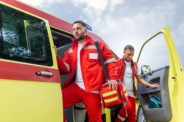 Enfermeira paramédica e médico de emergência na ambulância com kit um paramédico em pé na parte traseira de uma ambulância pelas portas abertas