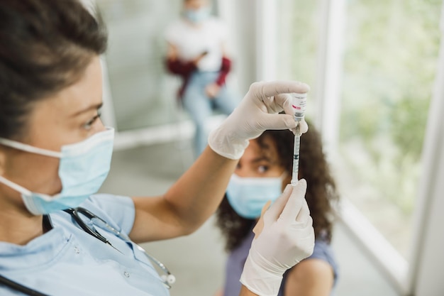 Enfermeira segurando seringa e fazendo dose de injeção de vacinação Covid-19 no ombro de paciente do sexo feminino usando máscara.