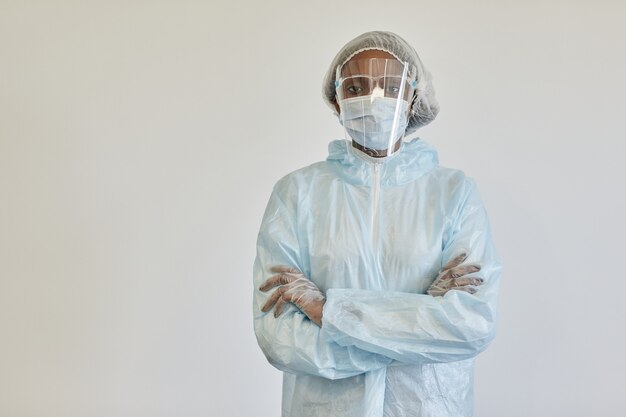 Foto enfermeira séria com roupa de ppe, máscara médica e luvas, cruzando os braços e olhando para a câmera isolada do branco