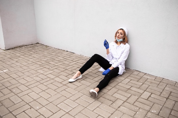 Foto enfermeira suja e cansada com cinzas no rosto sentada do lado de fora do hospital e fumando