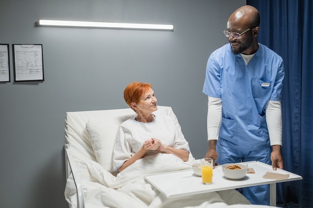 Enfermeira trazendo café da manhã para idosa que está deitada na cama na enfermaria do hospital