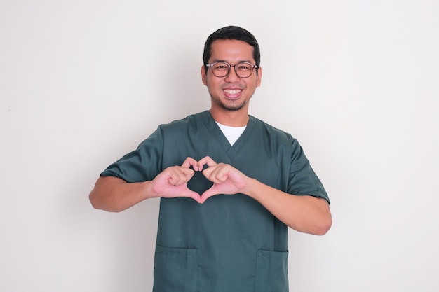 Enfermeiro asiático sorrindo feliz com a mão fazendo símbolo em forma de coração no peito
