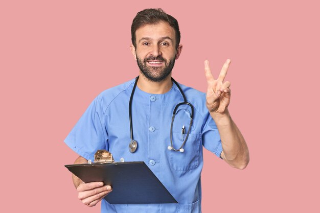 Enfermeiro hispânico com inventário mostrando o número dois com dedos.