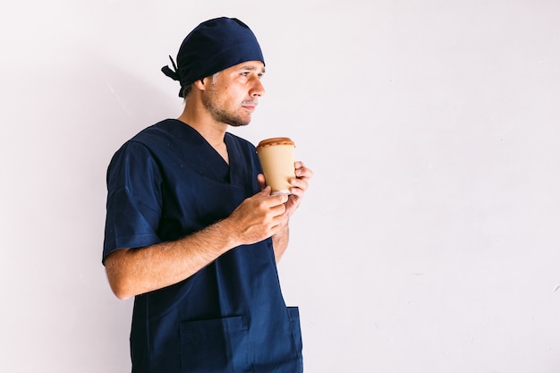 Enfermeiro, médico ou veterinário em uniforme azul escuro, olhando pela janela de um hospital, tomando café: conceito de medicina, hospital e saúde.