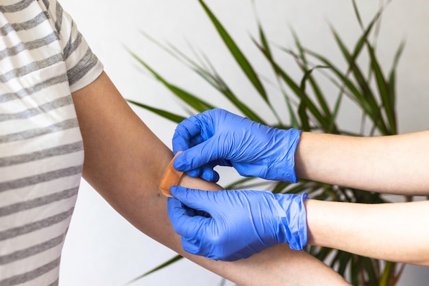 Enfermeiro ou médico em luvas de proteção de borracha azul, colocando bandagem adesiva no braço do jovem após a injeção da vacina