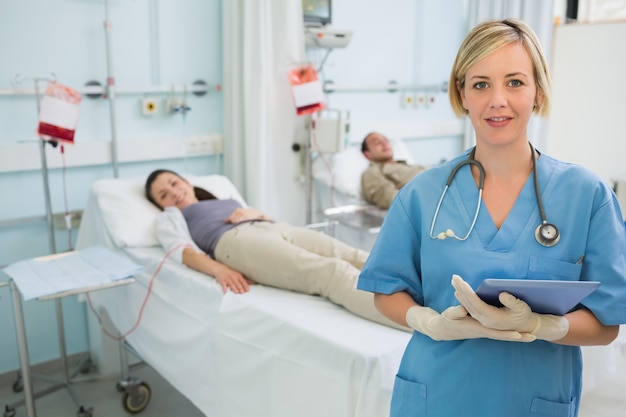 Enfermera al lado de pacientes sosteniendo un portapapeles