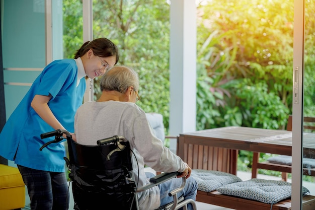 Foto la enfermera está apoyando a un anciano sentado en silla de ruedas caminando hacia la ventana