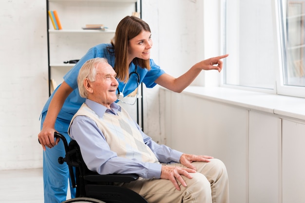 Enfermera apuntando a la ventana mientras habla con el viejo