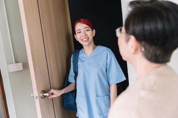 Enfermera asiática con batas cuidadora en el hogar visita a una mujer asiática mayor en la entrada con una sonrisa Cuidado de la salud en el hogar y concepto de hogar de ancianos