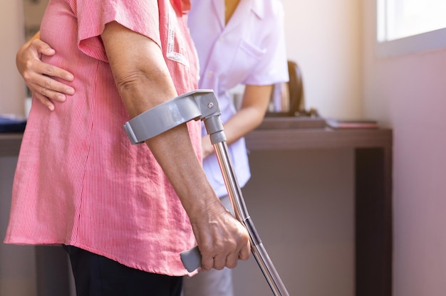 Enfermera ayudando a la mano de la mujer mayor con muletas tratando de caminar, concepto de hogar de ancianos de cuidado