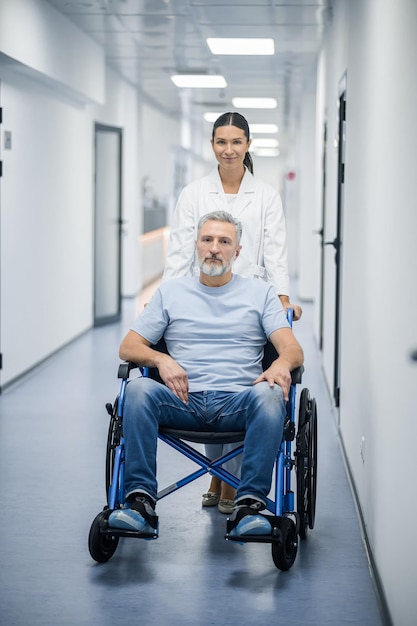 Enfermera de cabello oscuro que lleva la silla de ruedas con un paciente