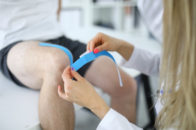 Enfermera con cinta adhesiva de kinesio en la rodilla del paciente. Protección de articulaciones y músculos en concepto deportivo