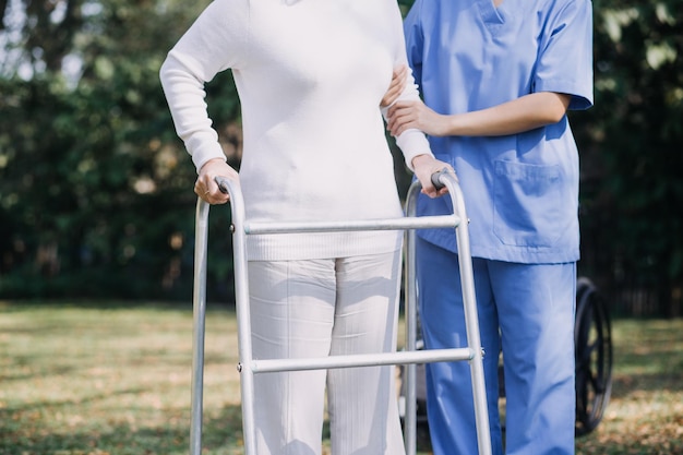 Enfermera cuidadora joven asiática apoya a un hombre mayor caminando al aire libre Una doctora especialista ayuda y cuida a un paciente anciano maduro que hace fisioterapia en un parque público en un hogar de ancianos