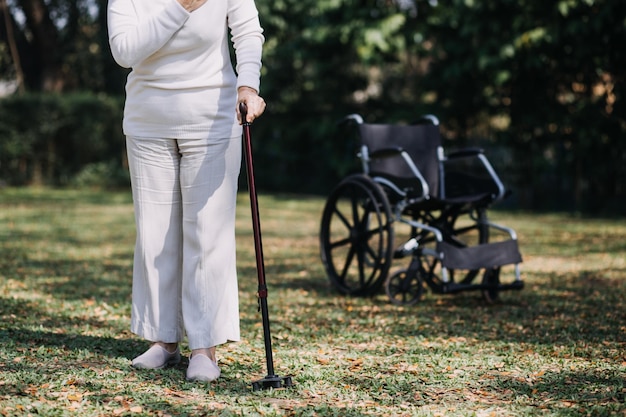 Enfermera cuidadora joven asiática apoya a un hombre mayor caminando al aire libre Una doctora especialista ayuda y cuida a un paciente anciano maduro que hace fisioterapia en un parque público en un hogar de ancianos