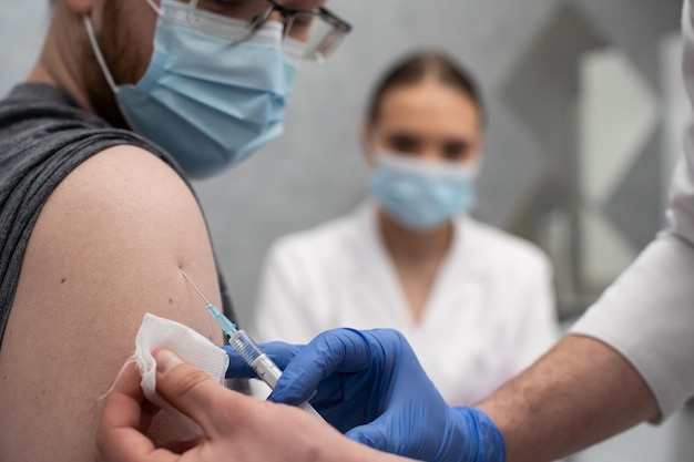 Una enfermera le da una inyección a un paciente con la vacuna COVID-19 Un consultorio de médicos estériles en una clínica privada Un joven pasante médico mira cómo inyectarse correctamente