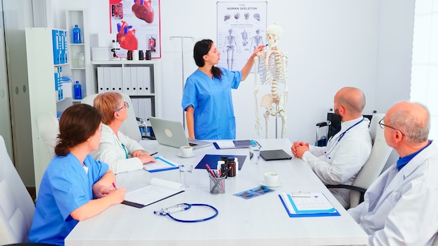 Enfermera dando una presentación frente al equipo de médicos sobre la anatomía humana con esqueleto. Terapeuta experto de la clínica hablando con colegas sobre la enfermedad, profesional de la medicina.