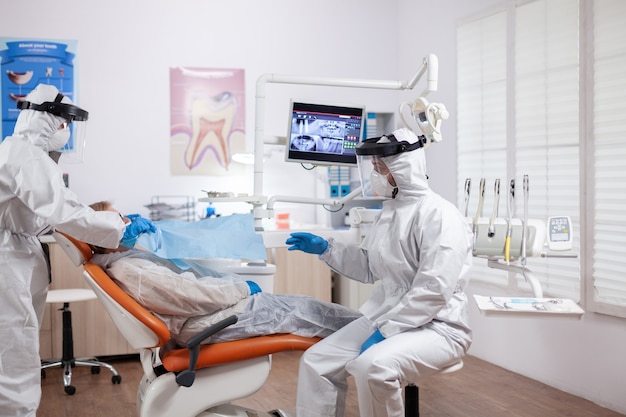 Enfermera dentista tomando la temperatura del paciente con traje de materiales peligrosos con termómetro digital