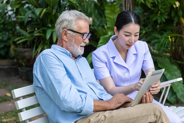 La enfermera le enseña a un anciano a usar una tableta en el jardín de un hogar de ancianos