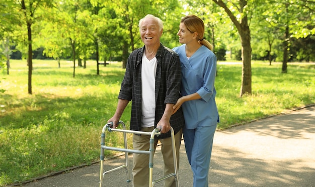 Enfermera feliz ayudando a un anciano con un andador en el parque
