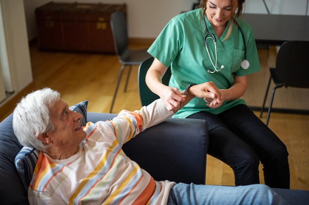 Enfermera feliz con un estetoscopio visitando a un anciano concepto de asistente médico doméstico doctora del sistema de salud médica poniendo un reloj inteligente en un anciano