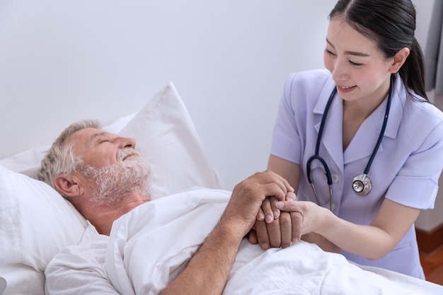 Enfermera feliz sosteniendo las manos de un anciano para motivarlo en el dormitorio en el hogar de ancianos