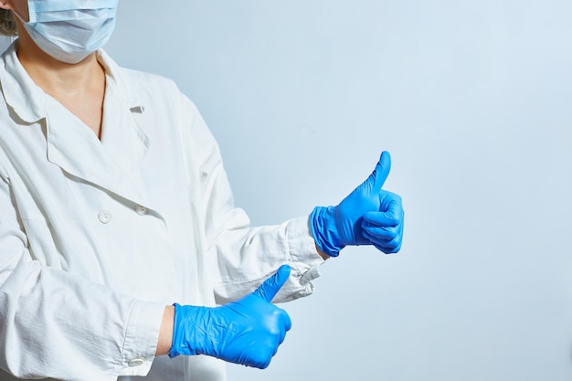 Una enfermera con guantes protectores y una bata blanca de laboratorio médico con una máscara facial muestra que todo está bien.