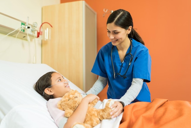 Enfermera hablando con un pequeño paciente en la cama del hospital durante el tratamiento