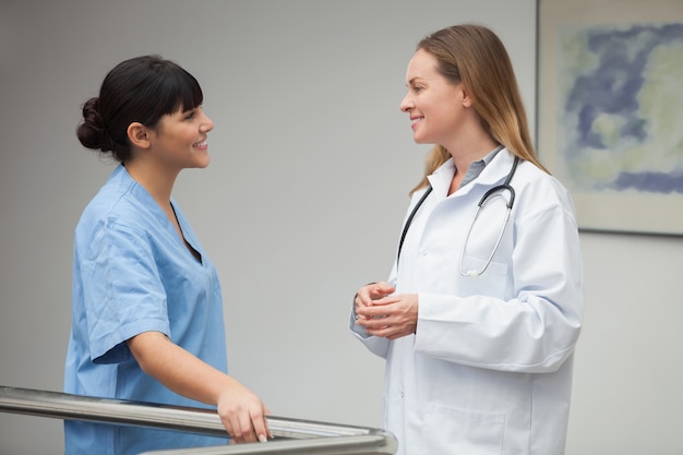Enfermera hablando y sonriendo con doctora en el pasillo del hospital