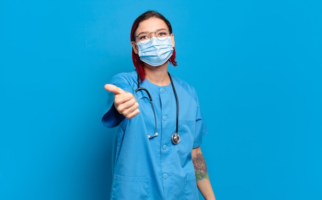 Enfermera joven atractiva pelirroja que se siente orgullosa, despreocupada, segura y feliz, sonriendo positivamente con los pulgares hacia arriba.