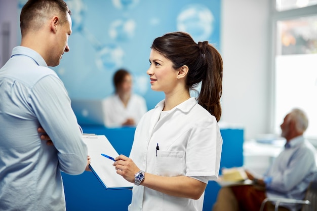 Enfermera joven hablando con un paciente masculino sobre sus datos en el registro médico en el hospital